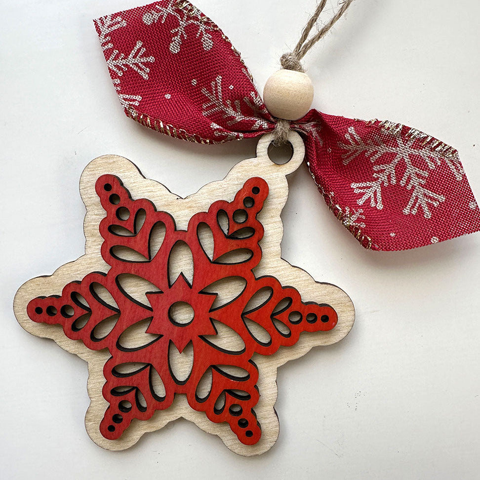 Wooden snowflake ornament with red cut-out design and a red ribbon on a white background