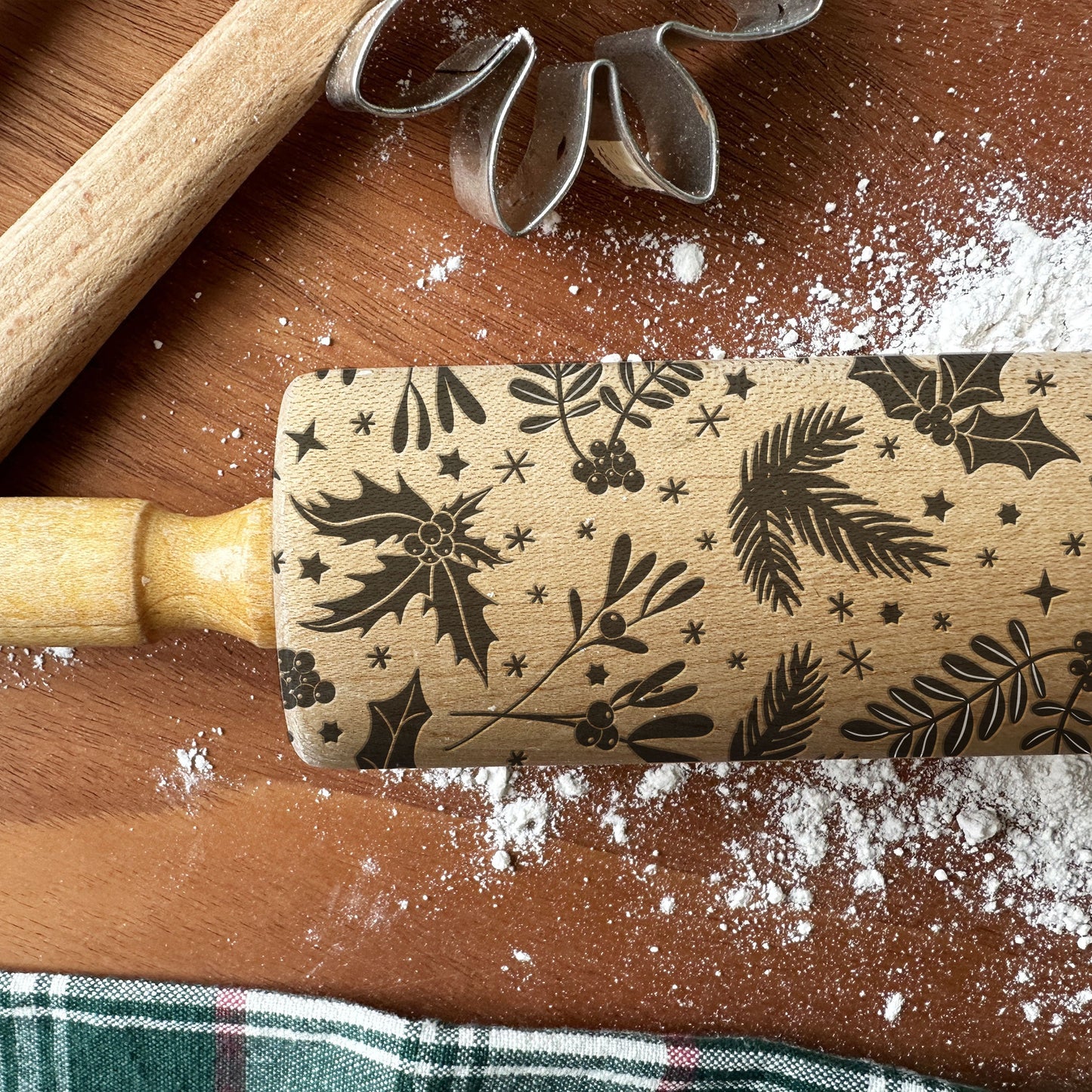 Rolling pin with floral pattern on a wooden surface with flour and cookie cutter.