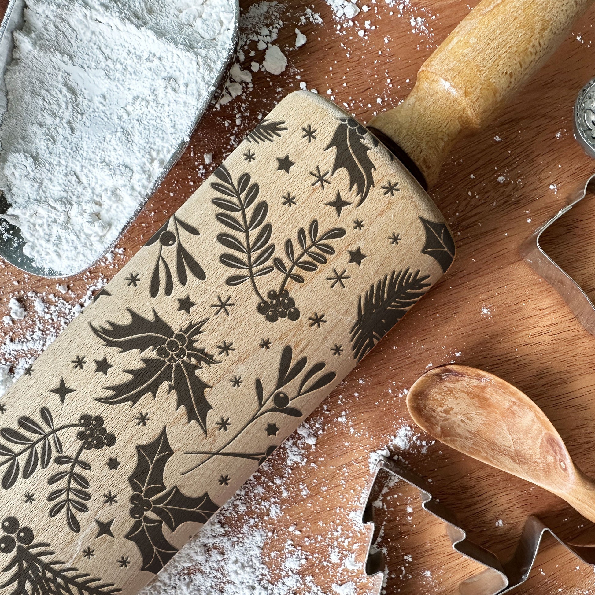 Wooden rolling pin with floral patterns and cookie cutters on a wooden surface with flour.