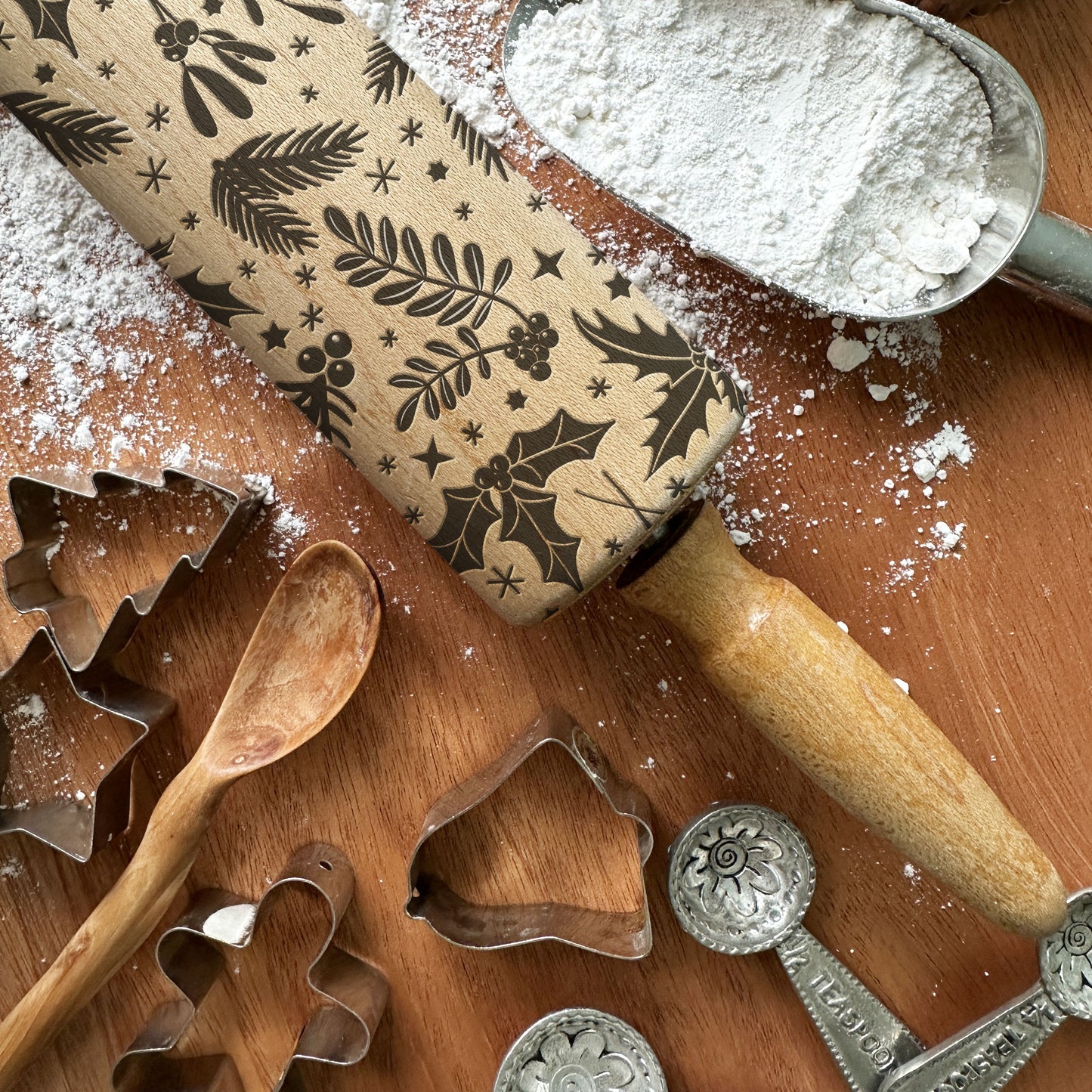 Wooden rolling pin with embossed patterns, cookie cutters, and flour on a wooden surface.