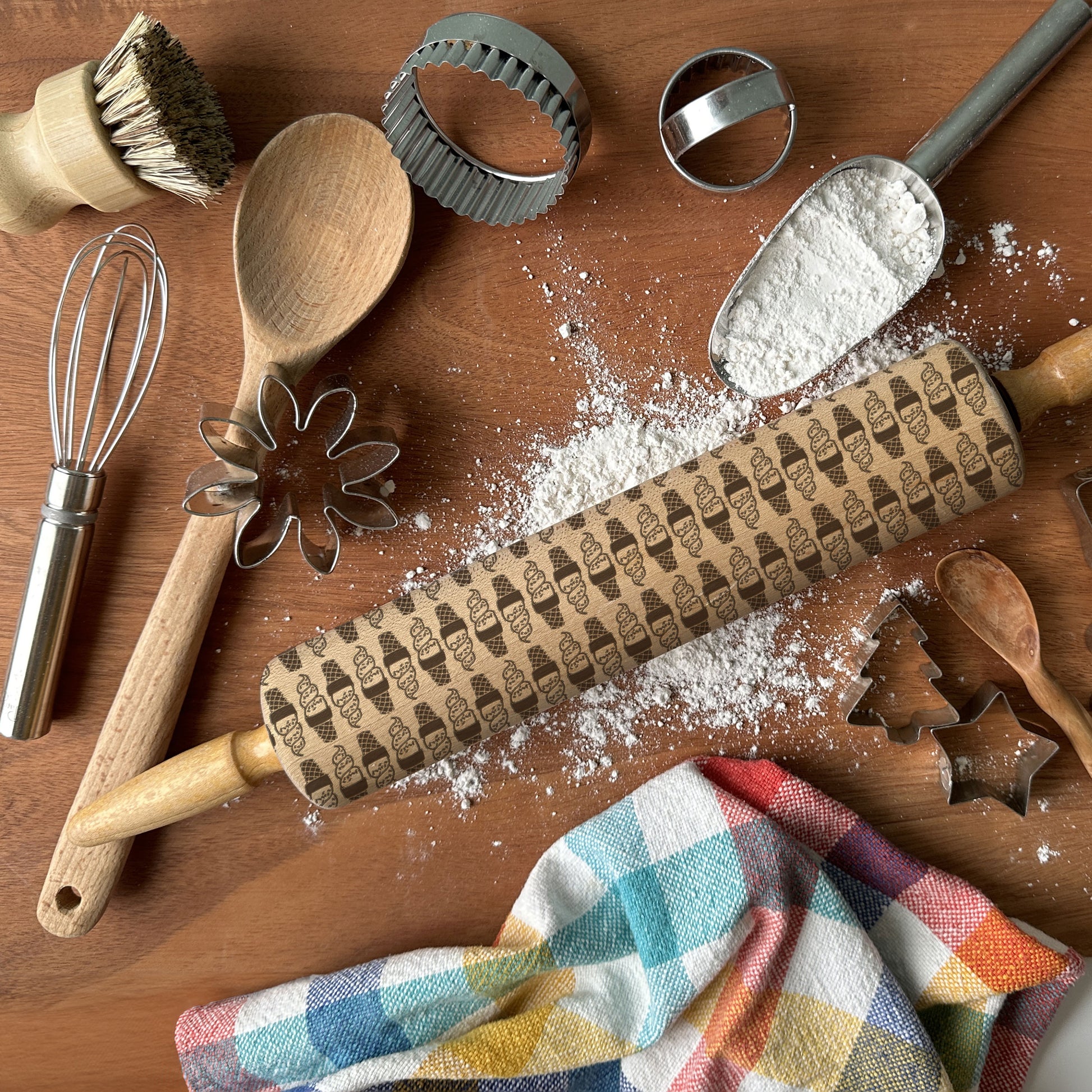 Baking tools including a rolling pin with embossed designs, flour, and utensils on a wooden surface.