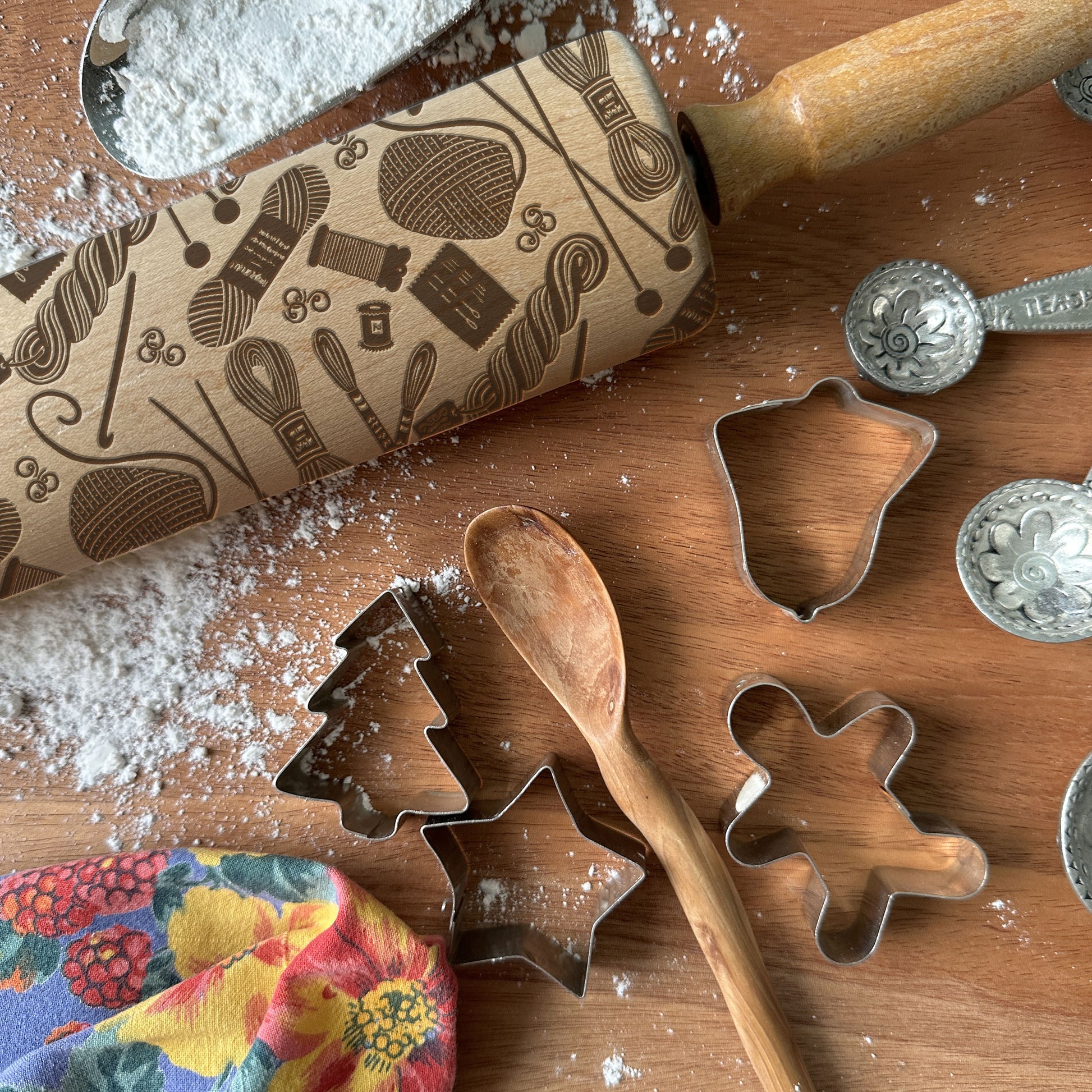 Baking tools including a rolling pin with embossed patterns, cookie cutters, and measuring spoons on a wooden surface.