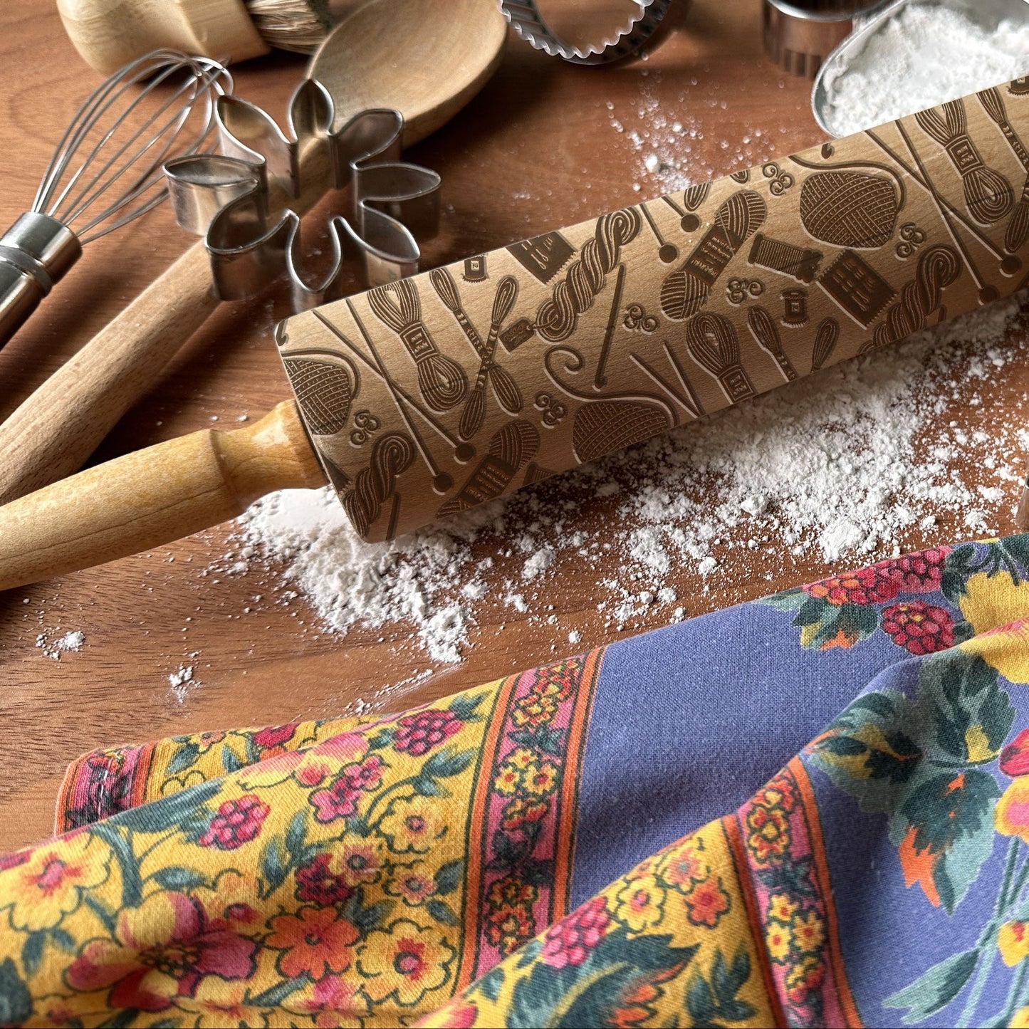 Decorative rolling pin with embossed patterns on a wooden surface with kitchen utensils and a colorful towel.