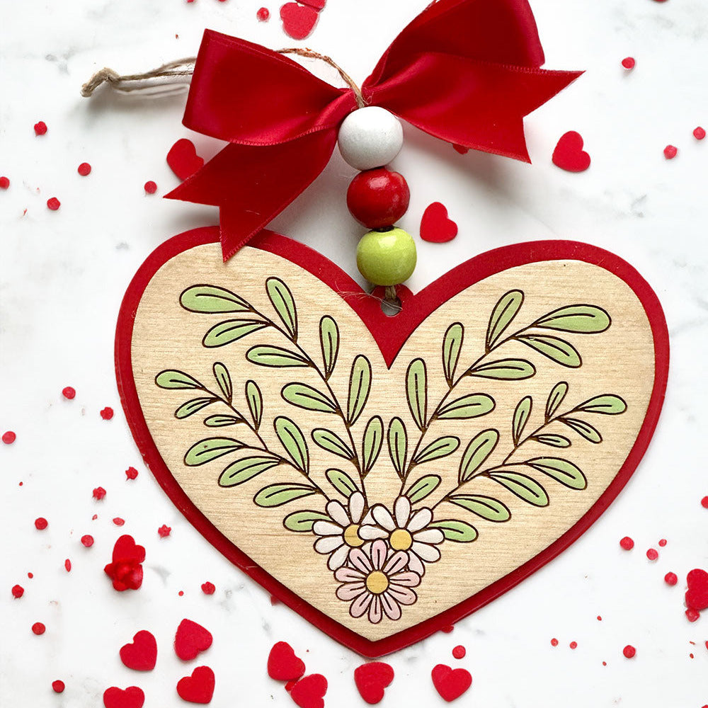 Decorative heart ornament with red bow and green leaves on a white background with red hearts.