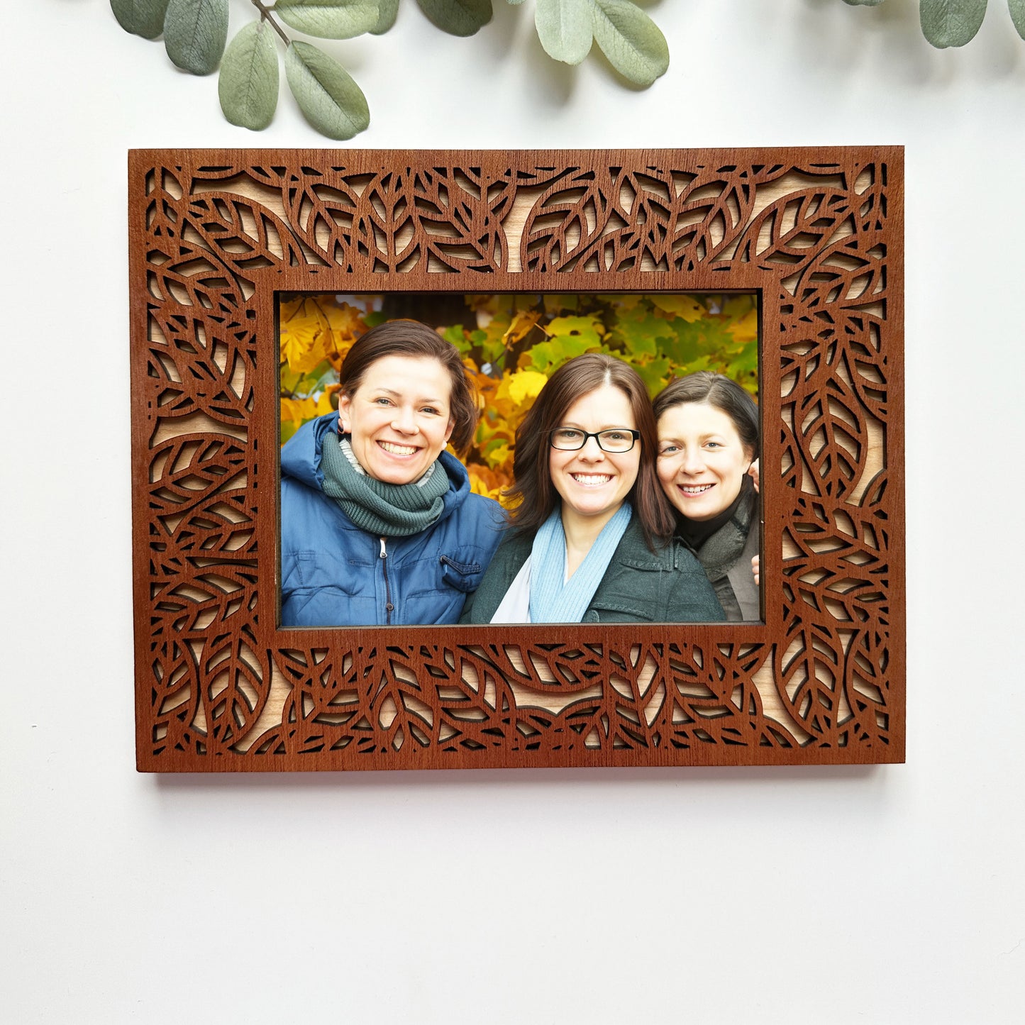Wooden photo frame with a decorative cut-out design, containing a photo of three people outdoors.