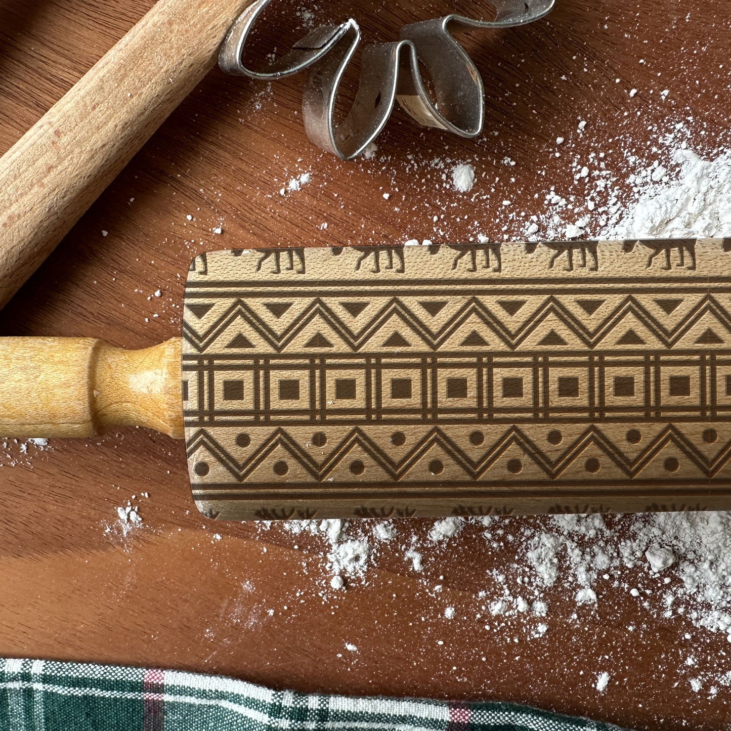 Decorative rolling pin with geometric pattern on a wooden surface with flour and cookie cutters.