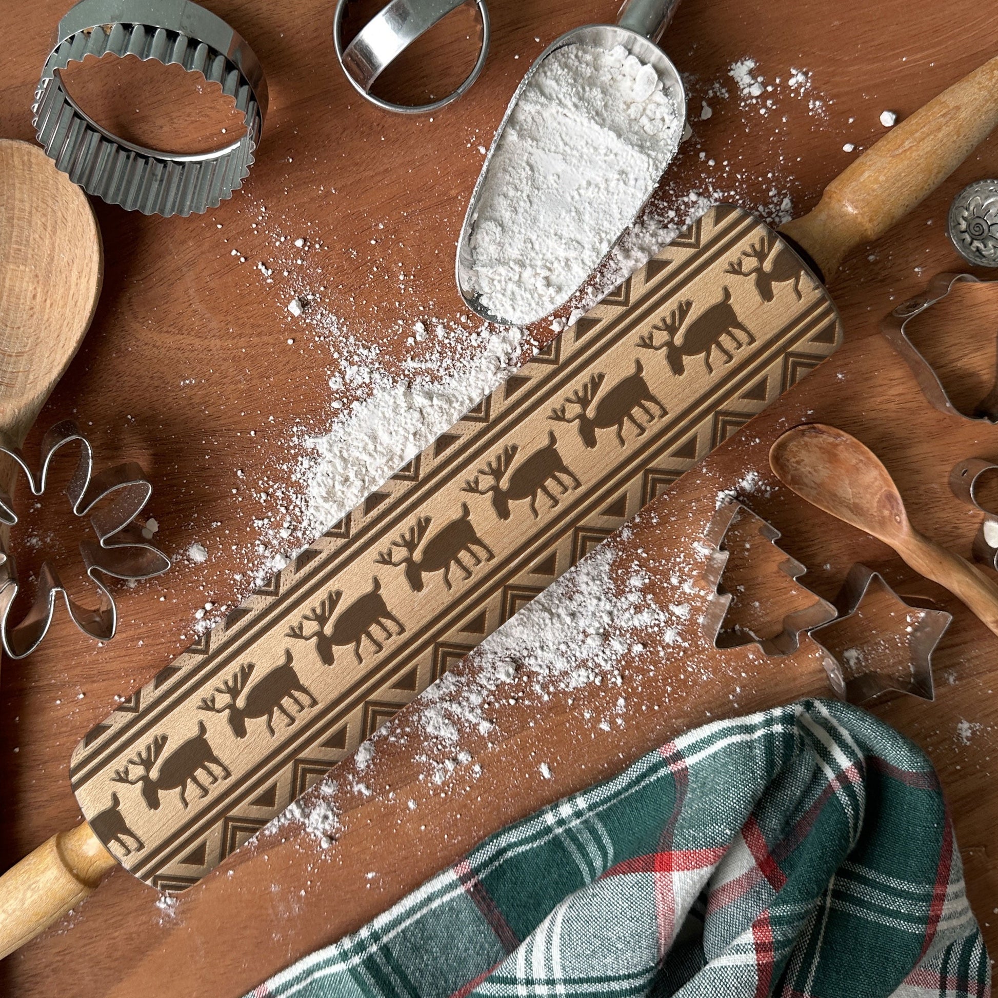 Wooden rolling pin with reindeer pattern on a wooden surface with flour and baking tools.