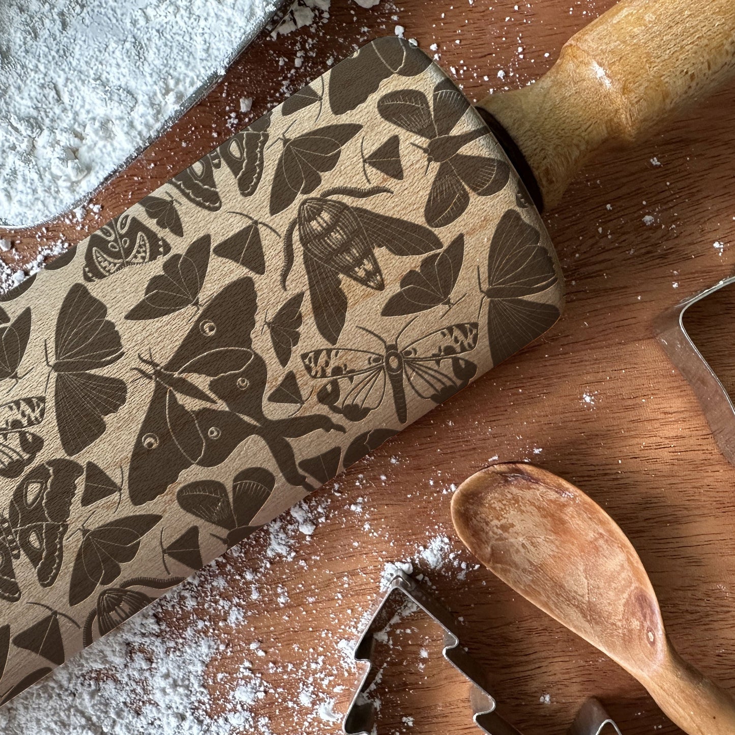 Butterfly-patterned rolling pin on a wooden surface with flour and cookie cutters.
