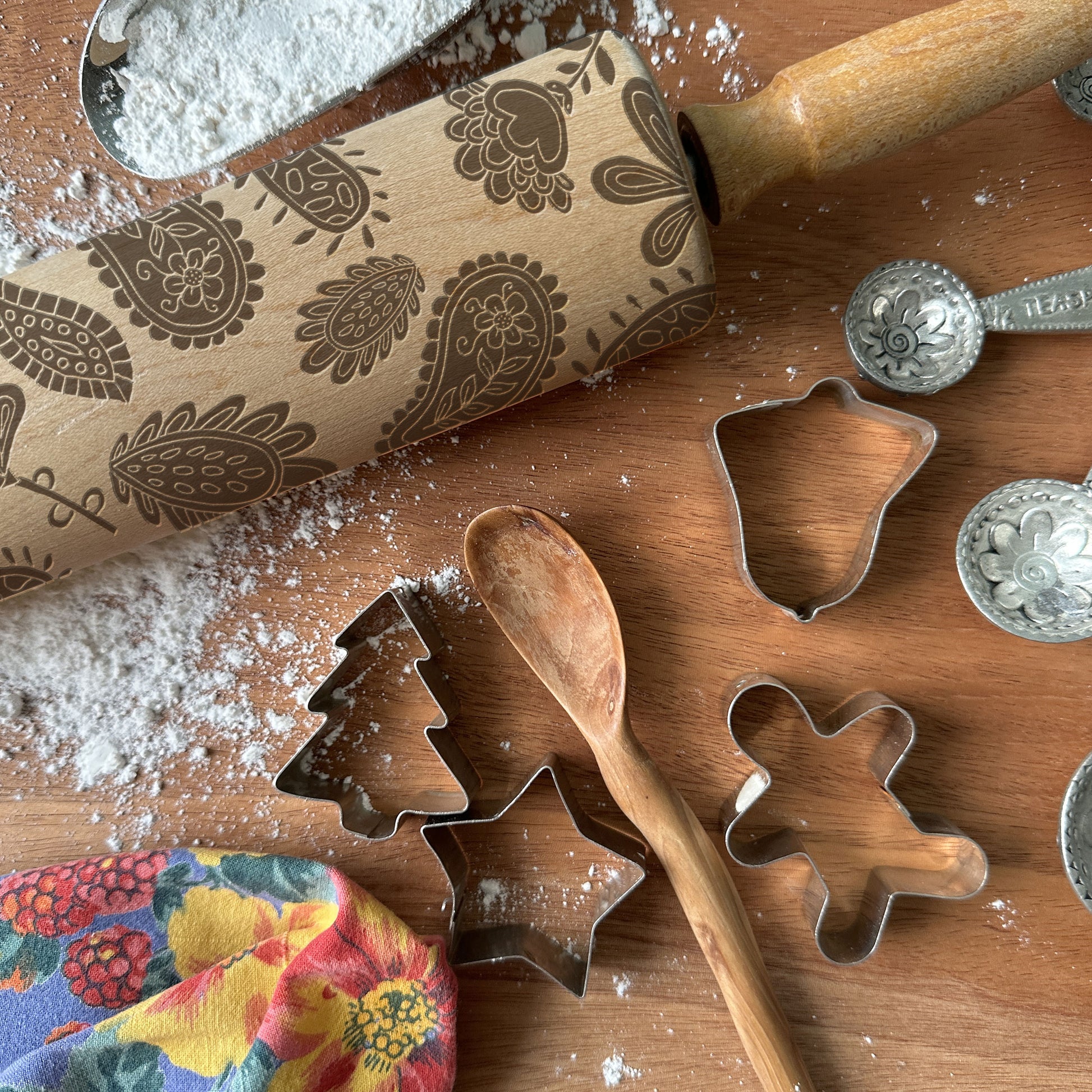 Wooden rolling pin with embossed patterns and metal cookie cutters on a wooden surface with flour.