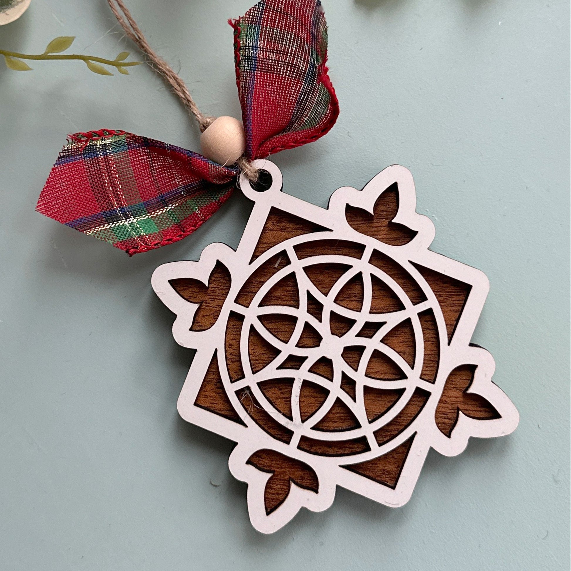 Stained glass Christmas ornament with a red ribbon on a light blue background