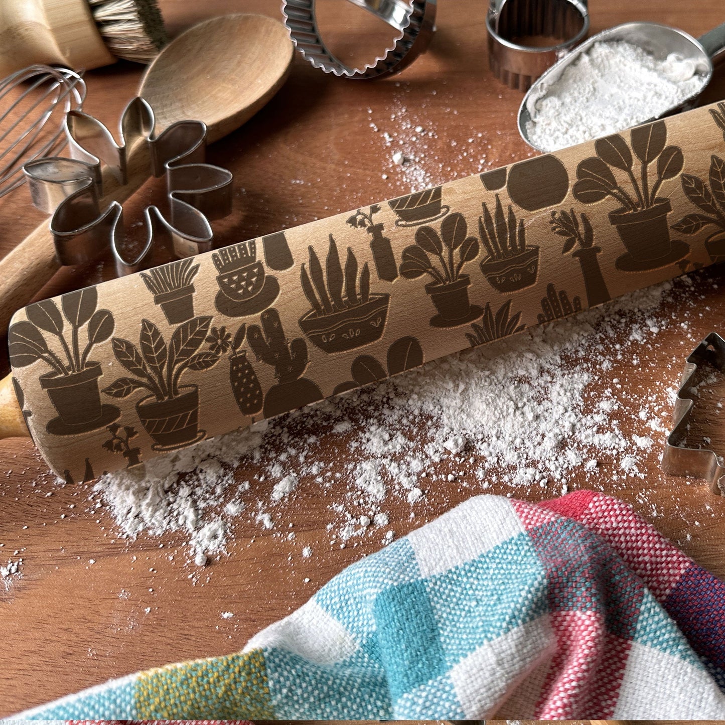 Rolling pin with plant pattern on a wooden surface with flour and kitchen tools.
