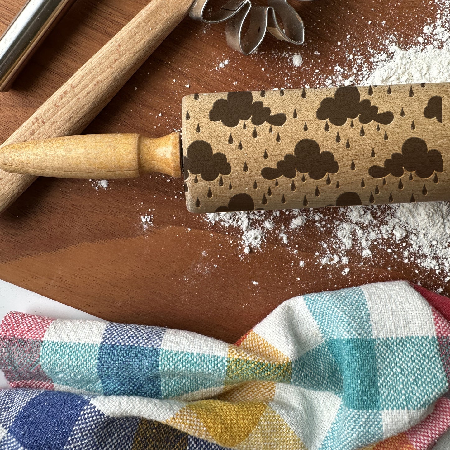 Wooden rolling pin with embossed cloud and raindrop pattern on a wooden surface with flour.