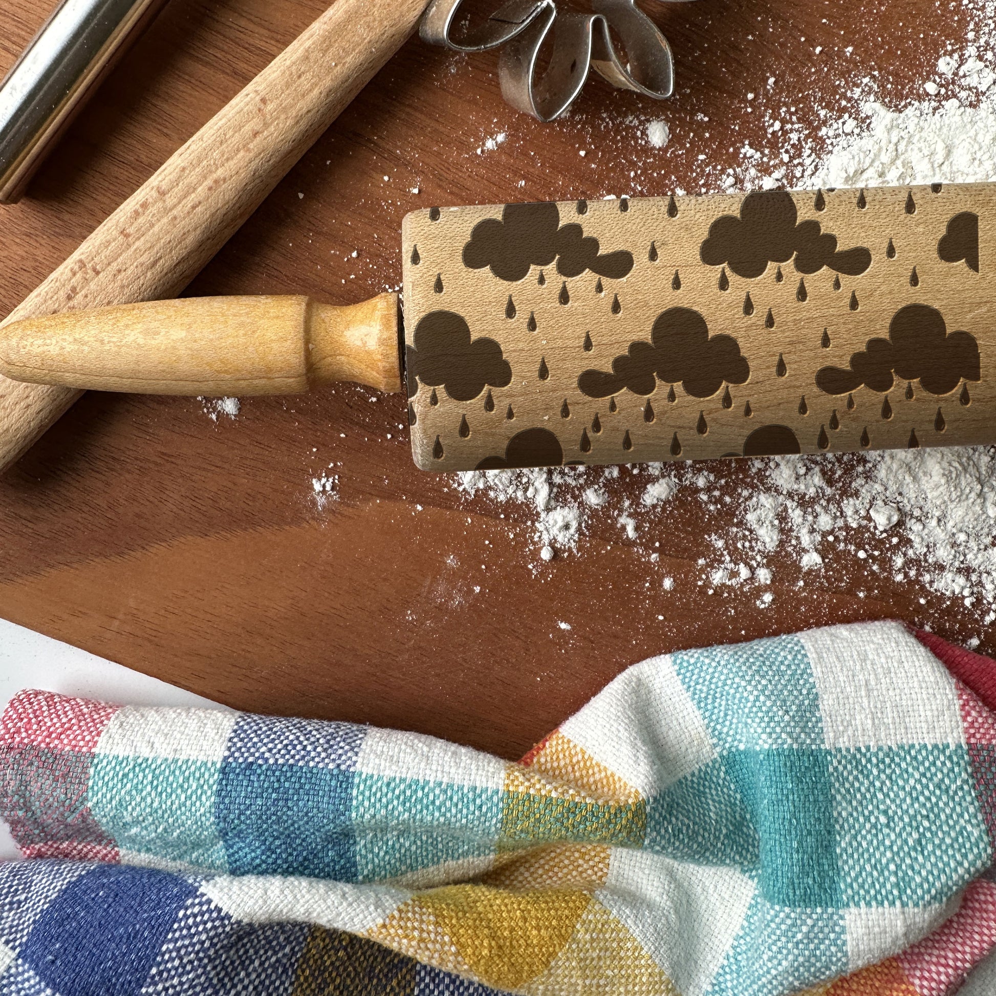 Wooden rolling pin with embossed cloud and raindrop pattern on a wooden surface with flour.