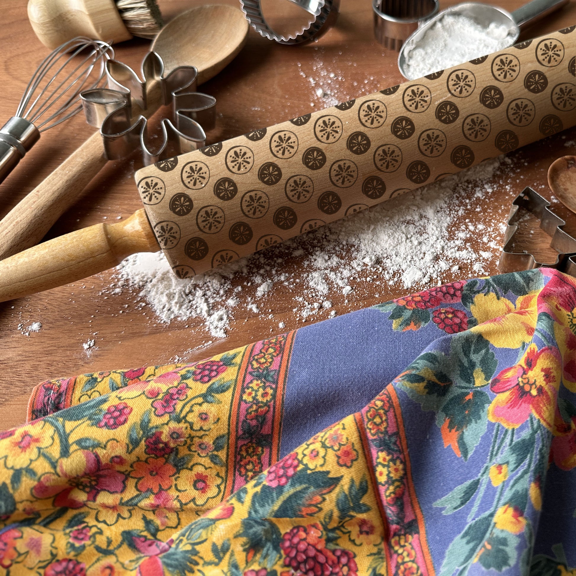 Rolling pin with pattern, flour, and colorful kitchen towel on a wooden surface
