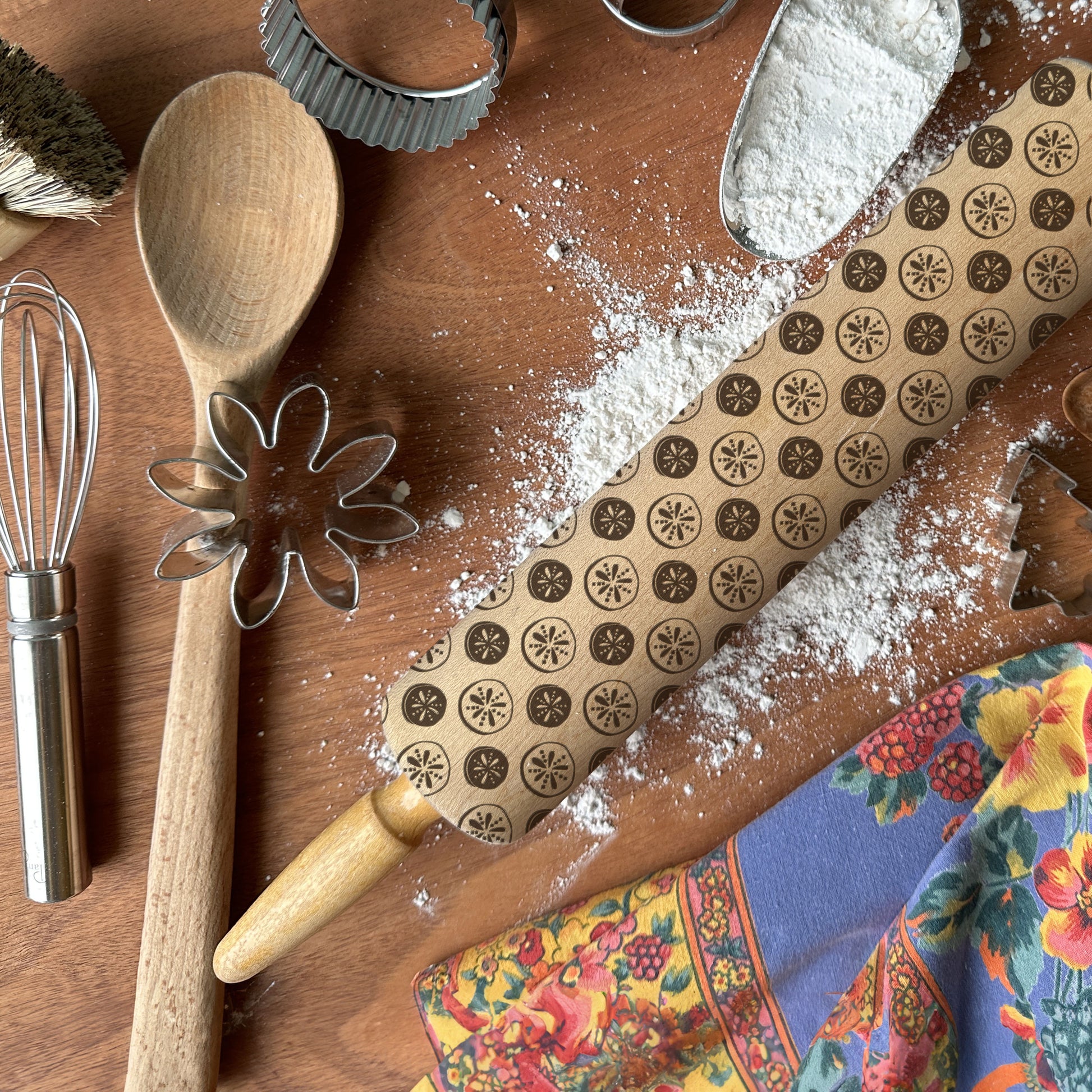 Baking tools including a wooden spoon, rolling pin, and cookie cutters on a wooden surface with flour.