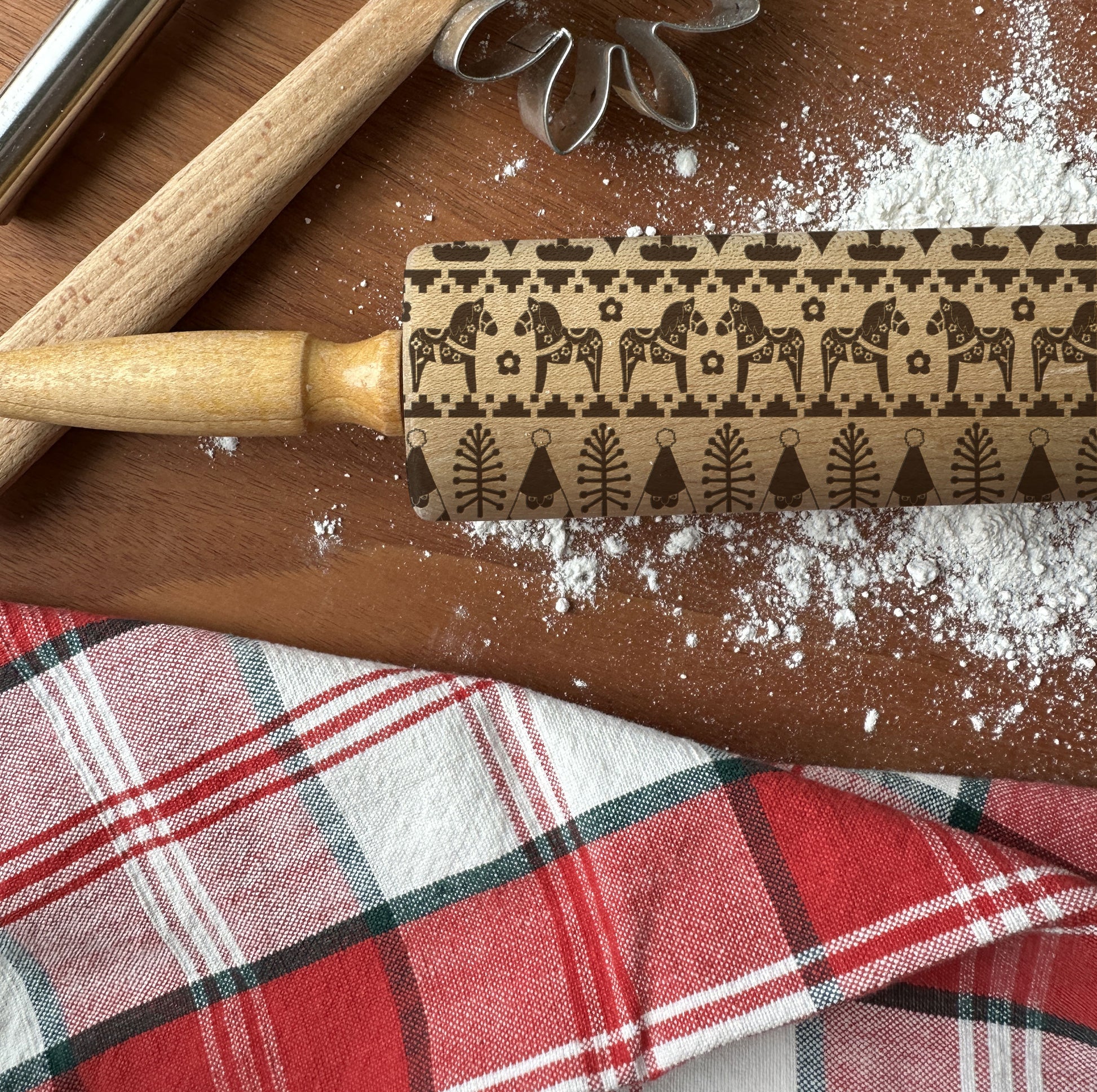 Rolling pin with horse pattern on a wooden surface with flour and plaid fabric.