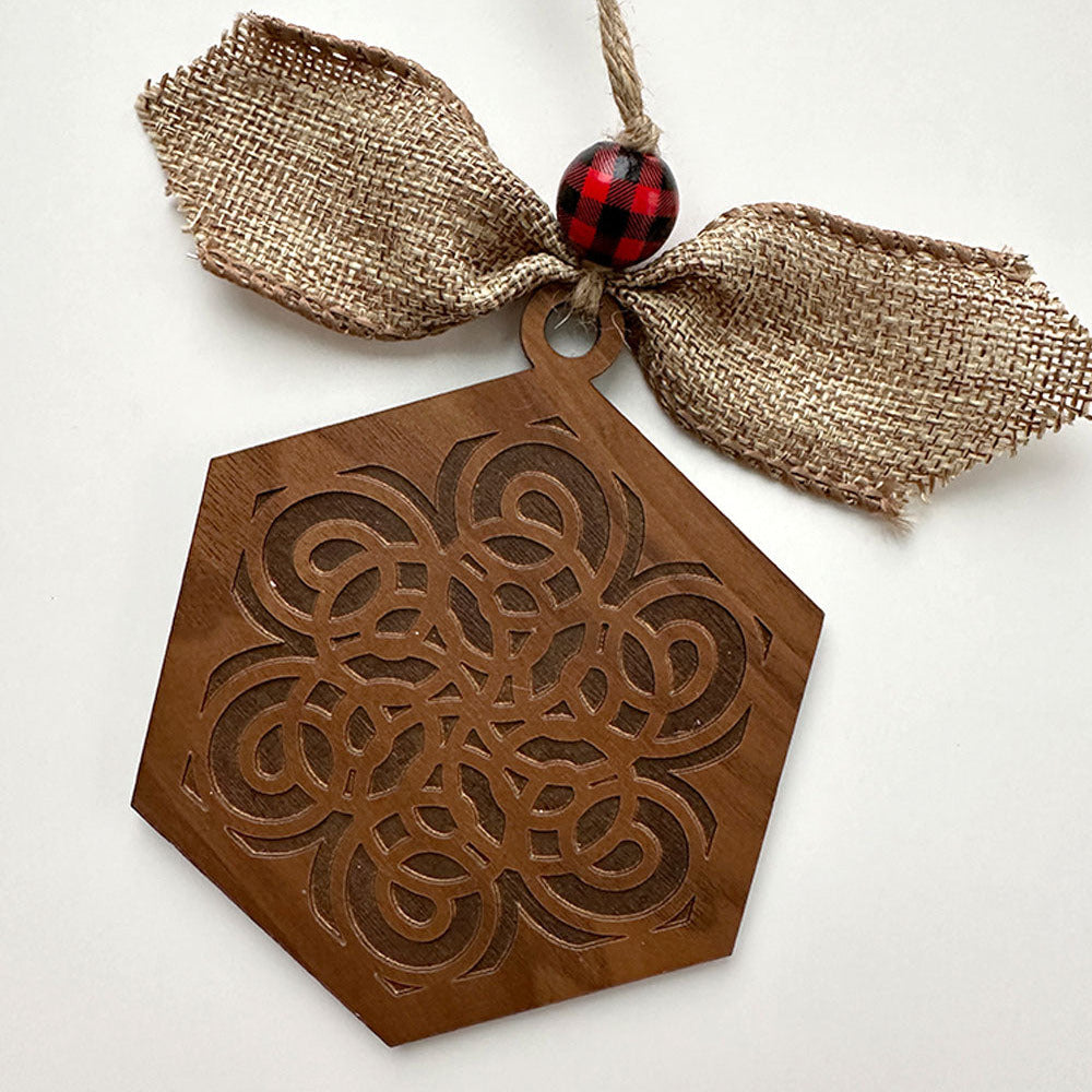 Decorative wooden ornament with intricate patterns, burlap ribbon, and red bead on a white background