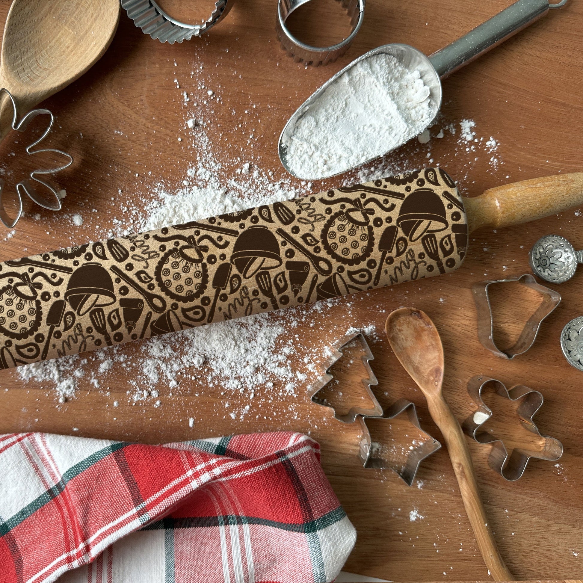 Wooden rolling pin with embossed designs on a wooden surface with flour and cookie cutters.