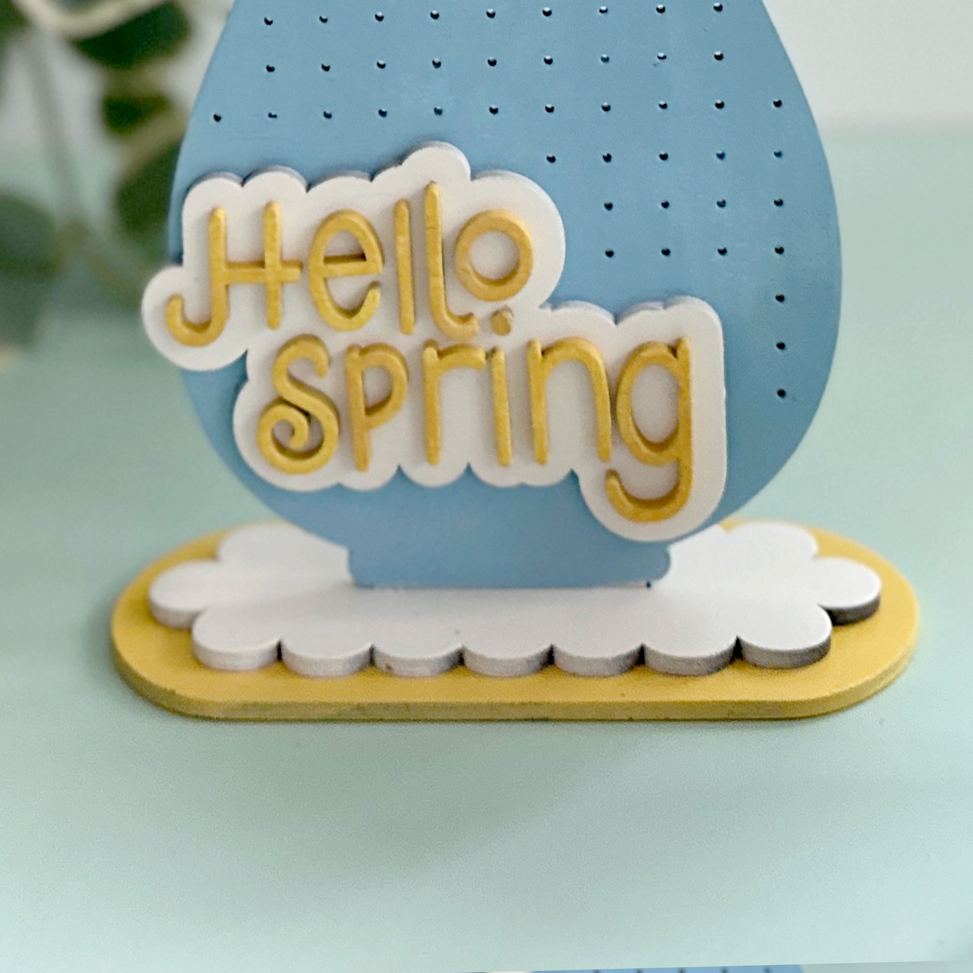Decorative sign with 'Hello Spring' text on a blue and yellow background