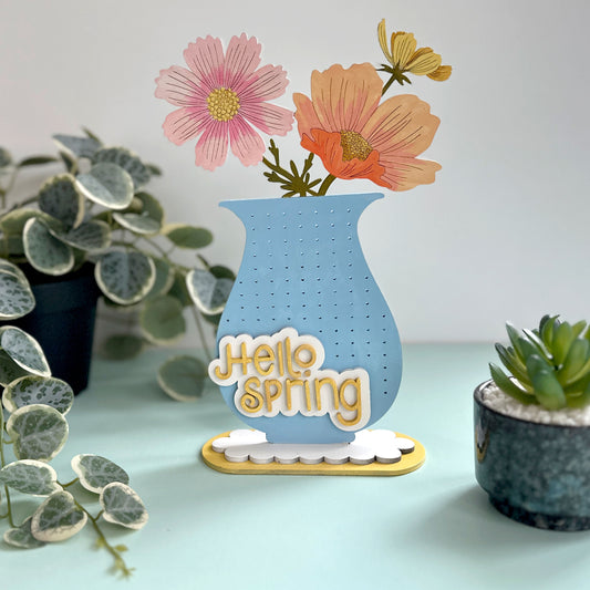 Decorative sign with 'Hello Spring' text and flowers on a light blue background