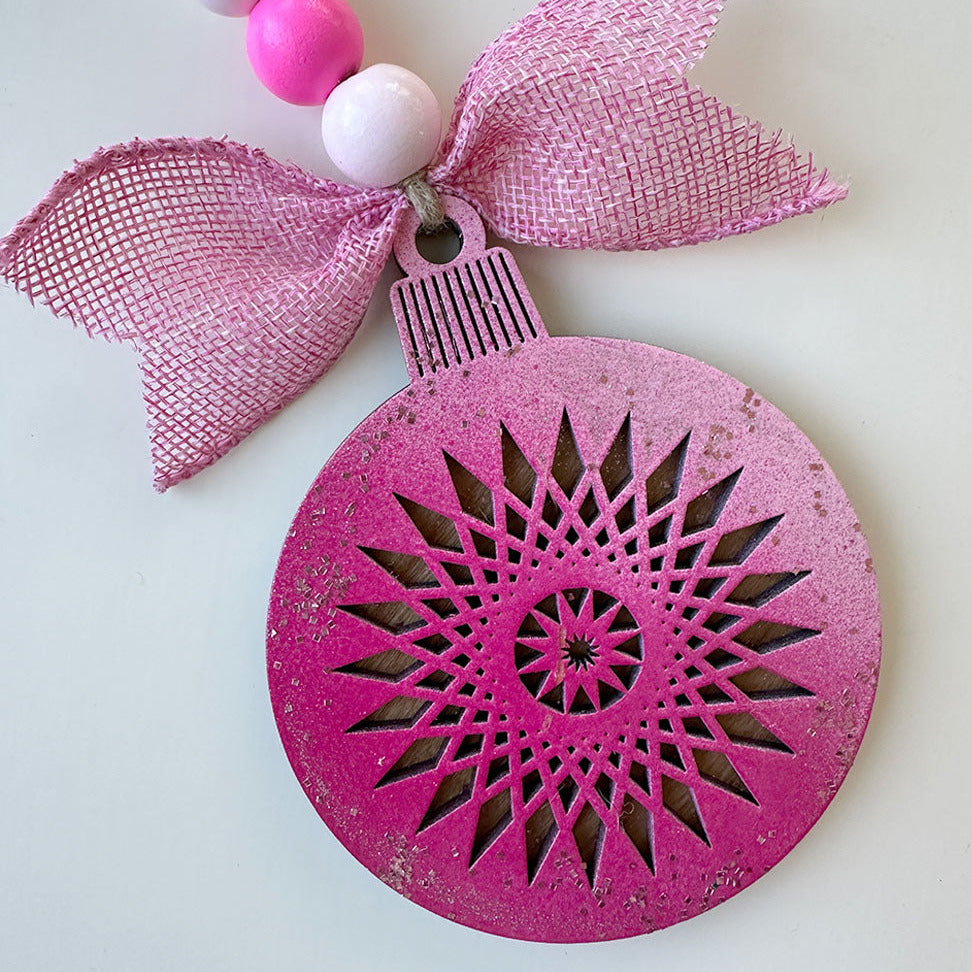 Pink decorative ornament with a starburst pattern and pink and white beads on a light gray background