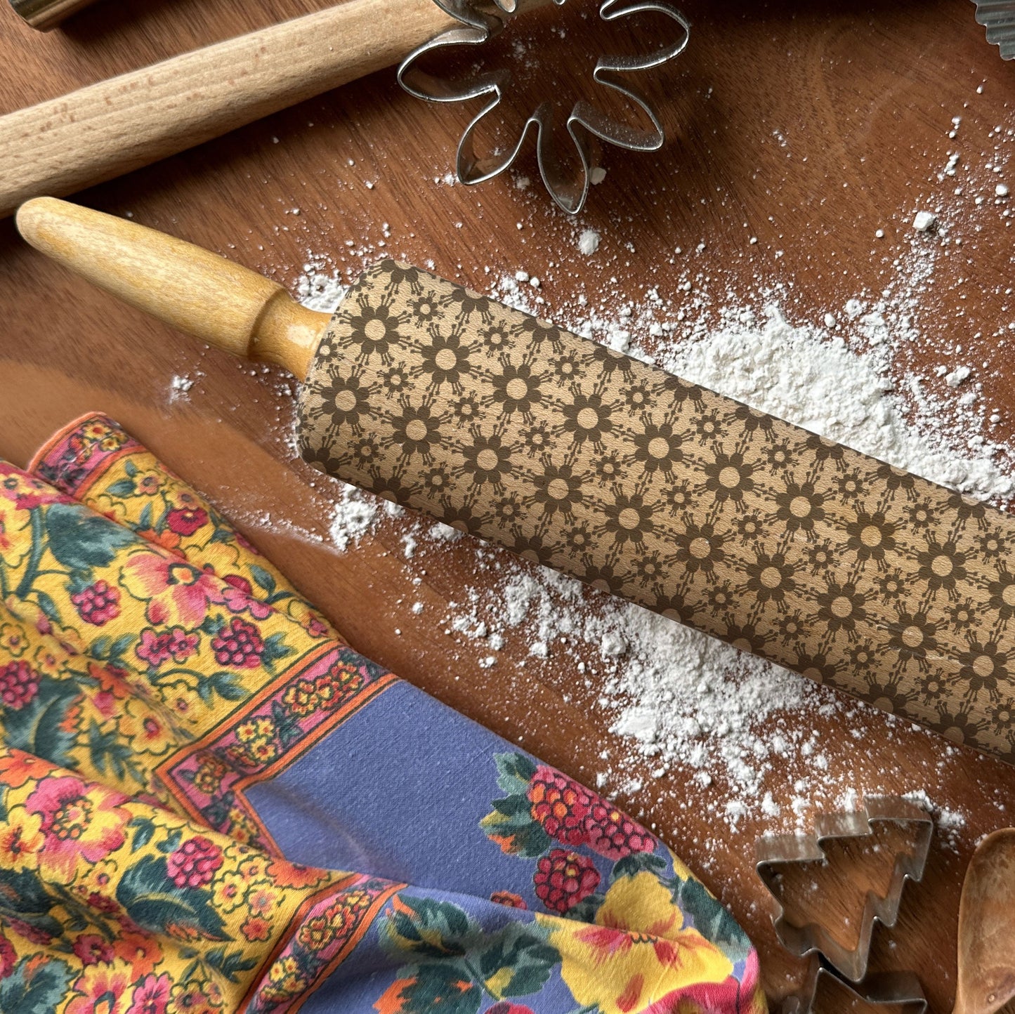 Decorative rolling pin with floral patterns on a wooden surface with flour and baking tools.