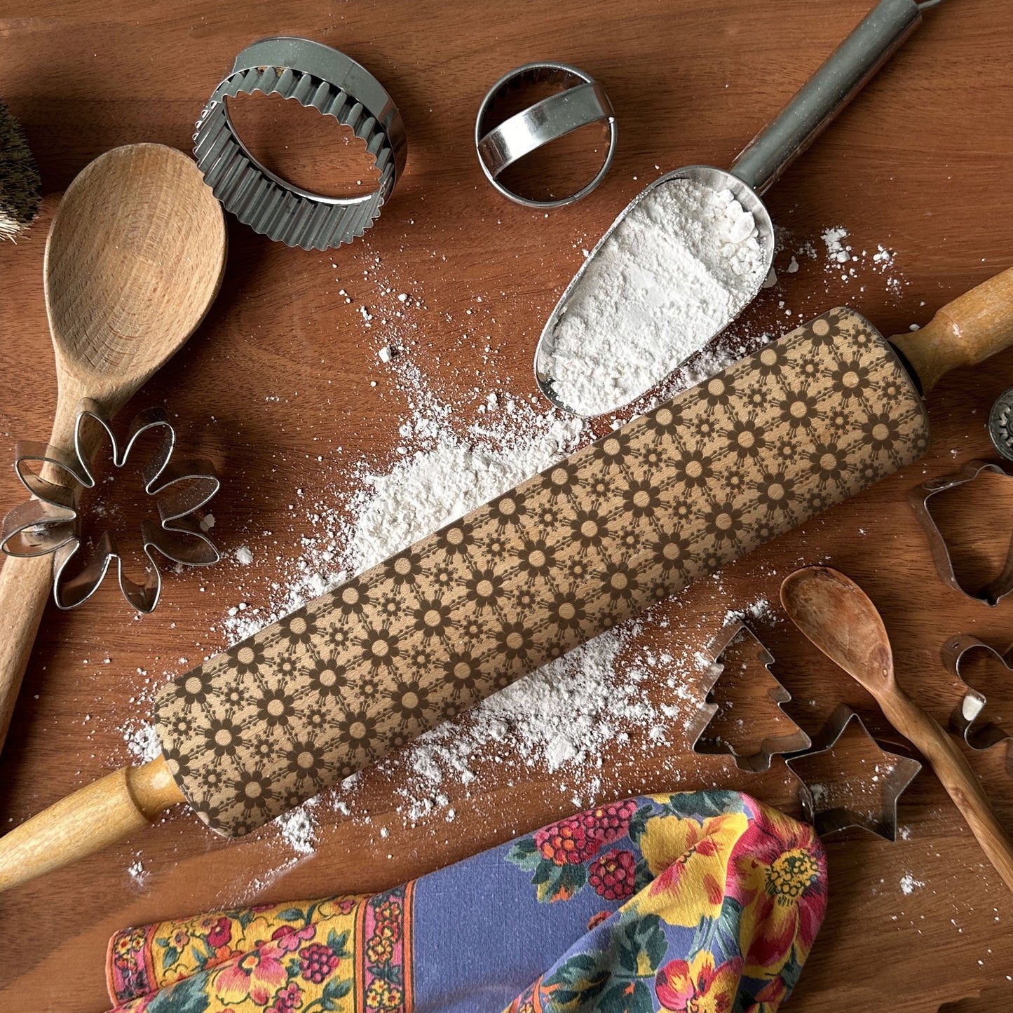 Baking tools including a rolling pin, wooden spoon, and cookie cutters on a wooden surface with flour.