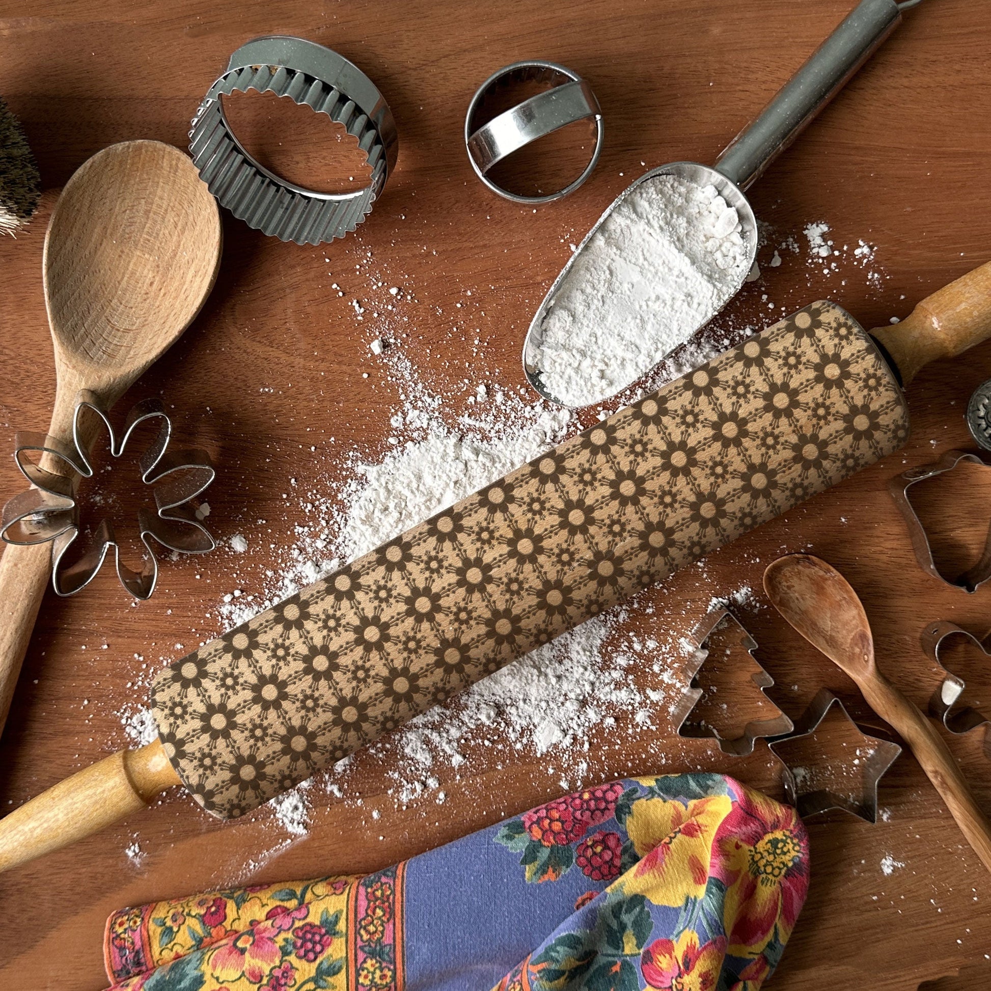 Baking tools including a rolling pin, wooden spoon, and cookie cutters on a wooden surface with flour.