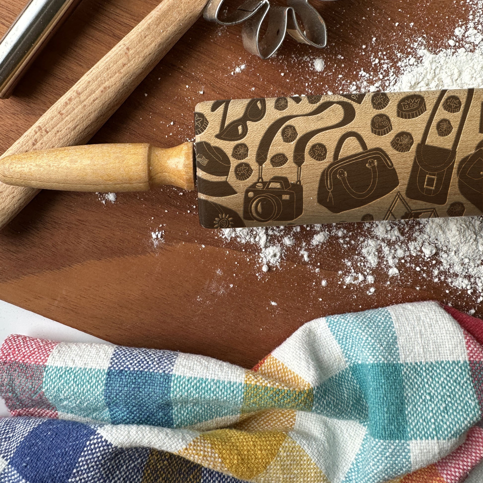 Rolling pin with decorative pattern on a wooden surface with flour and a checkered cloth.