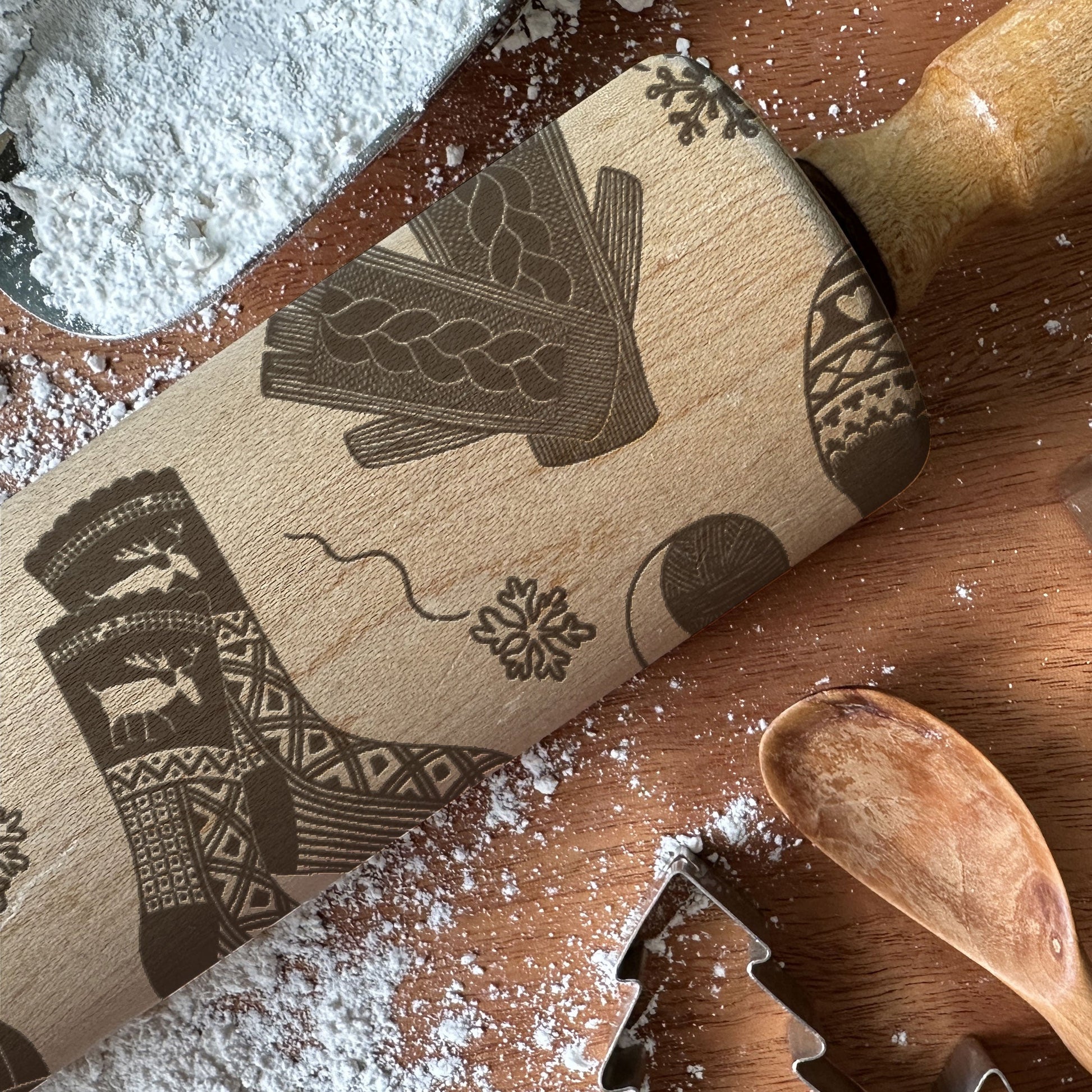 Wooden rolling pin with decorative patterns on a wooden surface with flour and cookie cutters.