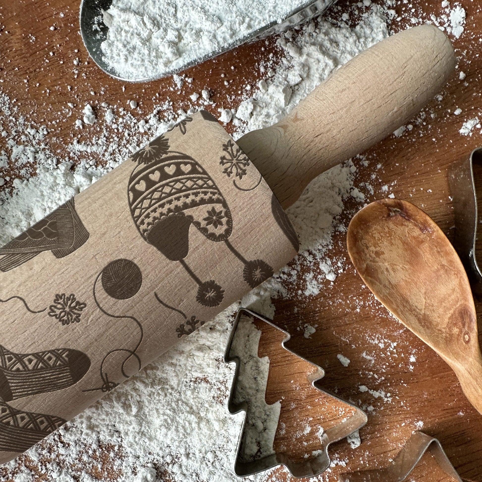 Wooden rolling pin with embossed patterns on a flour-dusted surface with cookie cutters.