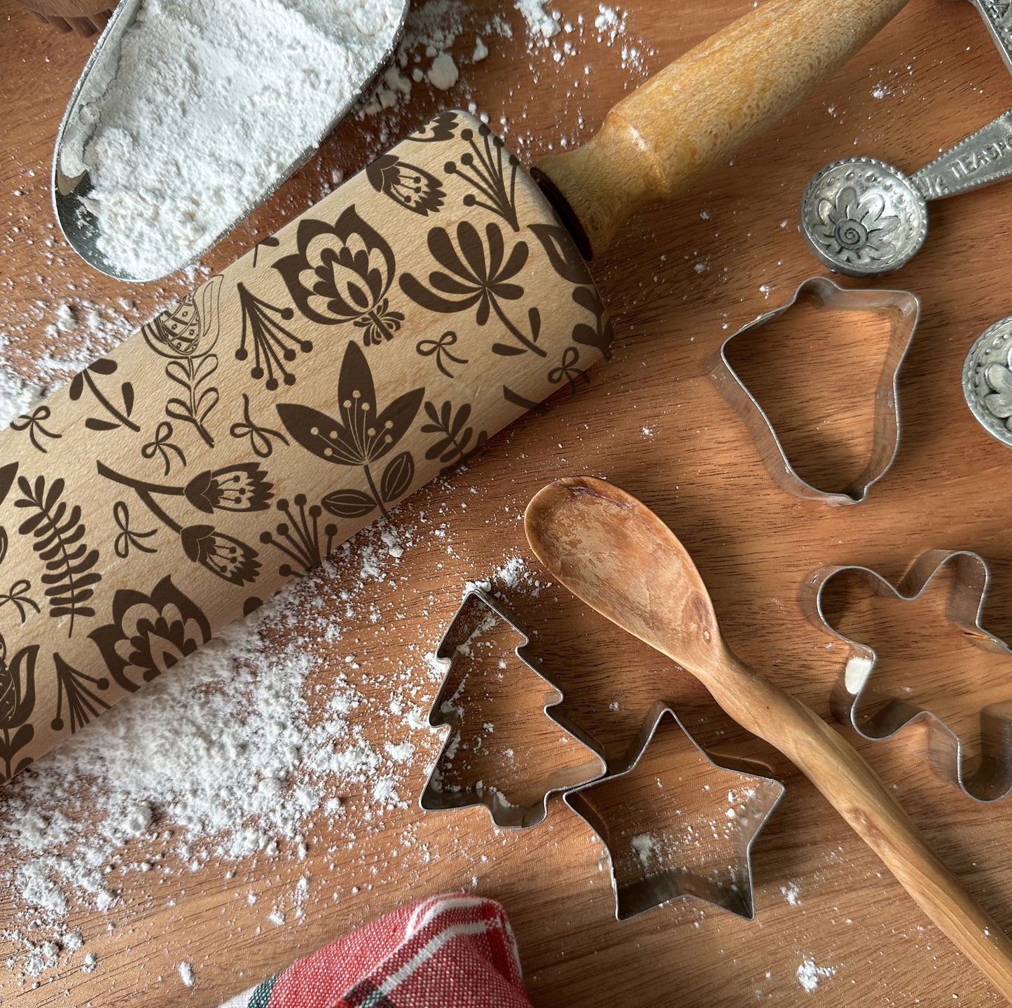 Baking tools including a patterned rolling pin, cookie cutters, and flour on a wooden surface.