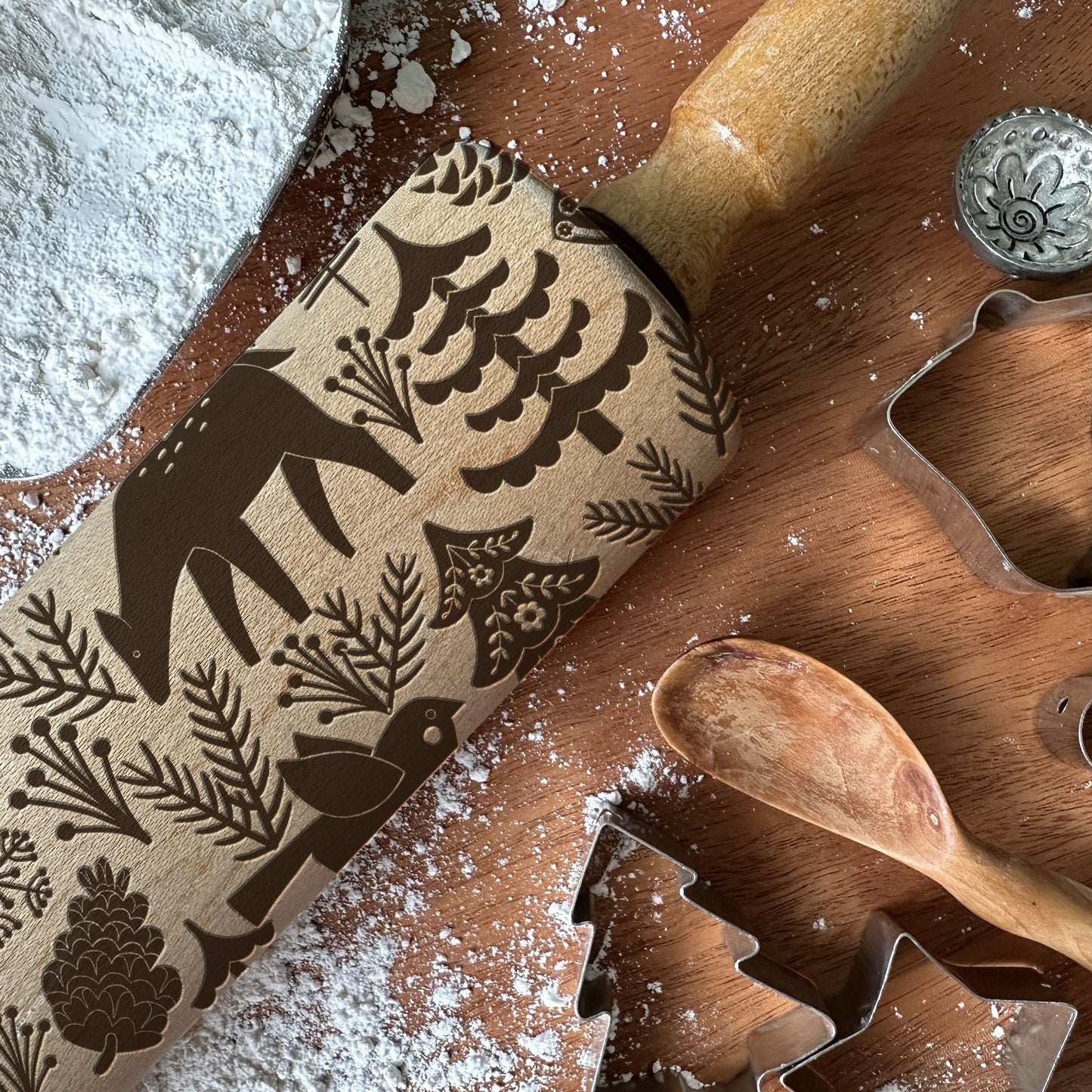 Wooden rolling pin with embossed designs on a wooden surface with cookie cutters and flour.